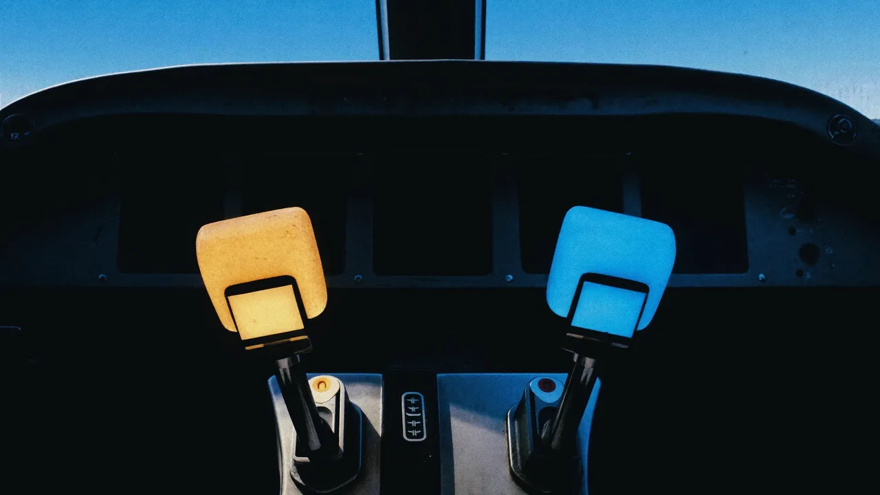 Two thrust levers in a cockpit set to the same position, one lit amber and one lit blue